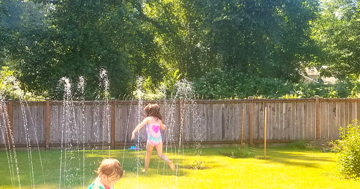 Kids playing in a sprinkler in the backyard