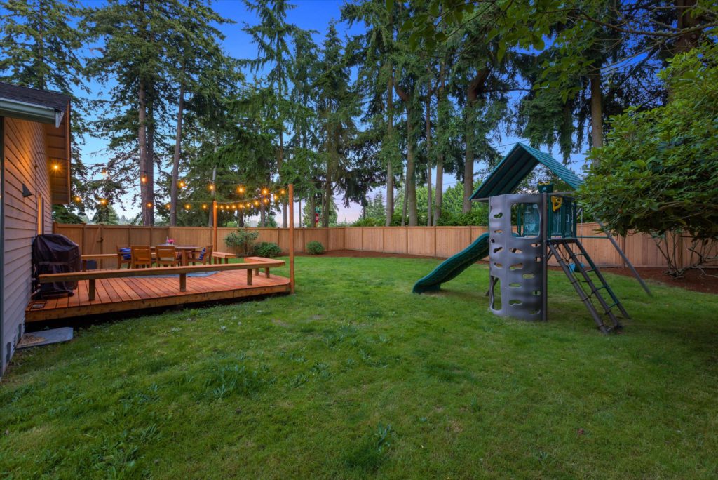 The backyard of an Edmonds home with fresh landscaping, a new deck and hung lights