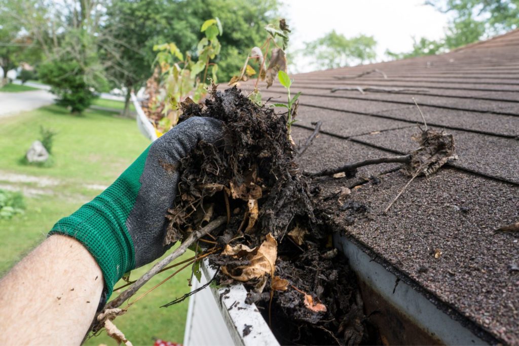 a hand cleaning dirt, debris and leaves out of a gutter